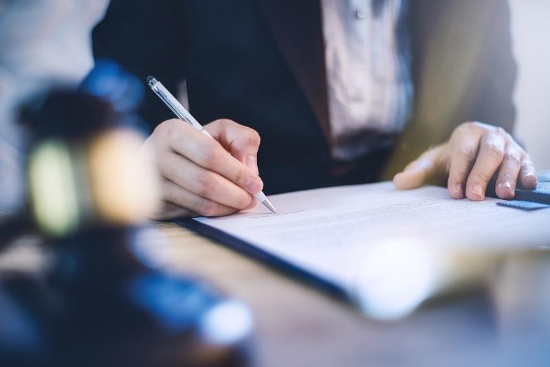 A photo of a white hand signing a Will