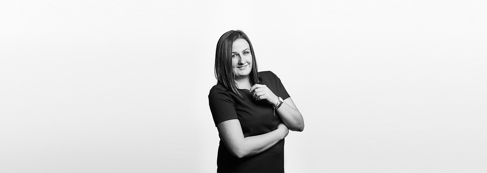 A grayscale photo of Danielle Carter, Associate Solicitor. She wears a dark short-sleeved blouse and has her arms crossed slightly, she is smiling.