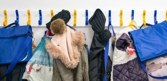 A row of school children's coats and bags hang on coat hooks.