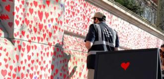 Two people dressed in 'Covid Memorial Wall' Hi-Vis jackets draw hearts on the wall