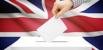 A hand places a paper in a ballot box in front of the Union Jack.
