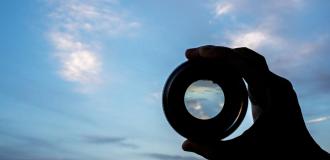 A hand holds up a magnifying lens to the sky 