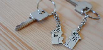 2 sets of keys lay on a wooden table. Each key has 1 half of a 'broken house' keyring that, when put together, make a complete house.