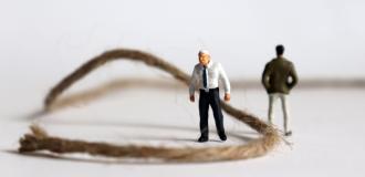 Two miniature figures of people, facing away from each other. A length of string separates them, coiling towards the lefthand side of the image.