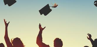 Silhouette of graduates throwing their mortar boards into the air against a blue sky.