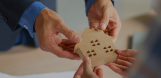 Two pairs of hands passing a small wooden house to each other