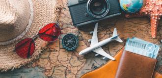 hat, model aeroplane, passports and other holiday themed items lying on a world map