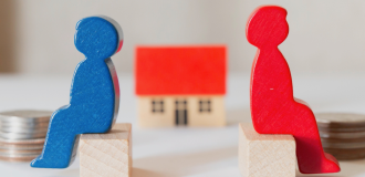 Wooden characters sat opposite each other with a small wooden house in between them. 