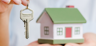 small toy house with a house key being held in front of it