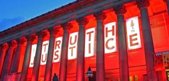 St George's Hall Liverpool, lit up red with "Truth" and "Justice" banner behind the buildings columns. 