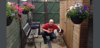 An image of Lee Arnold against a grey background. Lee is a white bald-headed man. He is wearing a red tshirt, crouching next to a dog. He's smiling and seems happy.  