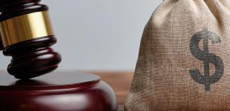 A gavel and a hessian bag with a dollar sign on a wooden table.