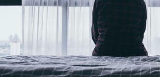 Silhouette of a person sat on a bed facing a window