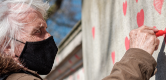 An elderly person drawing a red heart on the National Covid Memorial Wall