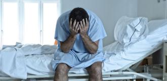 A man sits on a hospital bed with his head in his hands. 