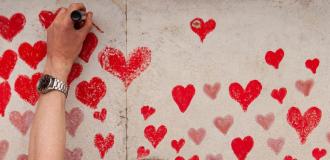 A white hand colours in a red heart on the National Covid Memorial Wall