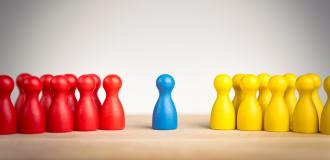 A group of red game pieces are standing opposite a group of yellow game pieces. A single blue game piece stands between the two groups.