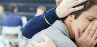 A man comforting a woman as she cries into a tissue.