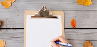 A person writing on a piece of paper surrounded in autumn coloured leaves