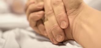 A person holds the hand of their loved one as they lay in a hospital bed