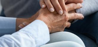 two people dressed in blue sit together holding hands. They are comforting and supporting one another