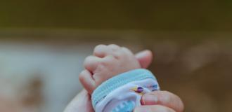 A baby's hand being held by its parent's hand.