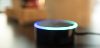 An out-of-focus image of an Alexa in the foreground with a living room in the background.