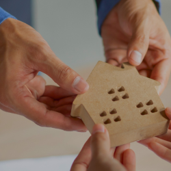 Two pairs of hands passing a small wooden house to each other