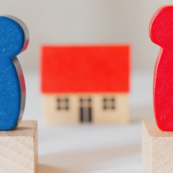 Wooden characters sat opposite each other with a small wooden house in between them. 