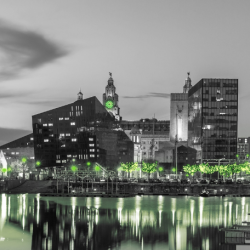 Black-and-white photo of a city at night with selective green lights on buildings and streets, creating a dramatic, modern mood.
