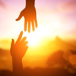 Two silhouetted hands reach toward each other from the top and bottom of the image in front of a sunrise. 